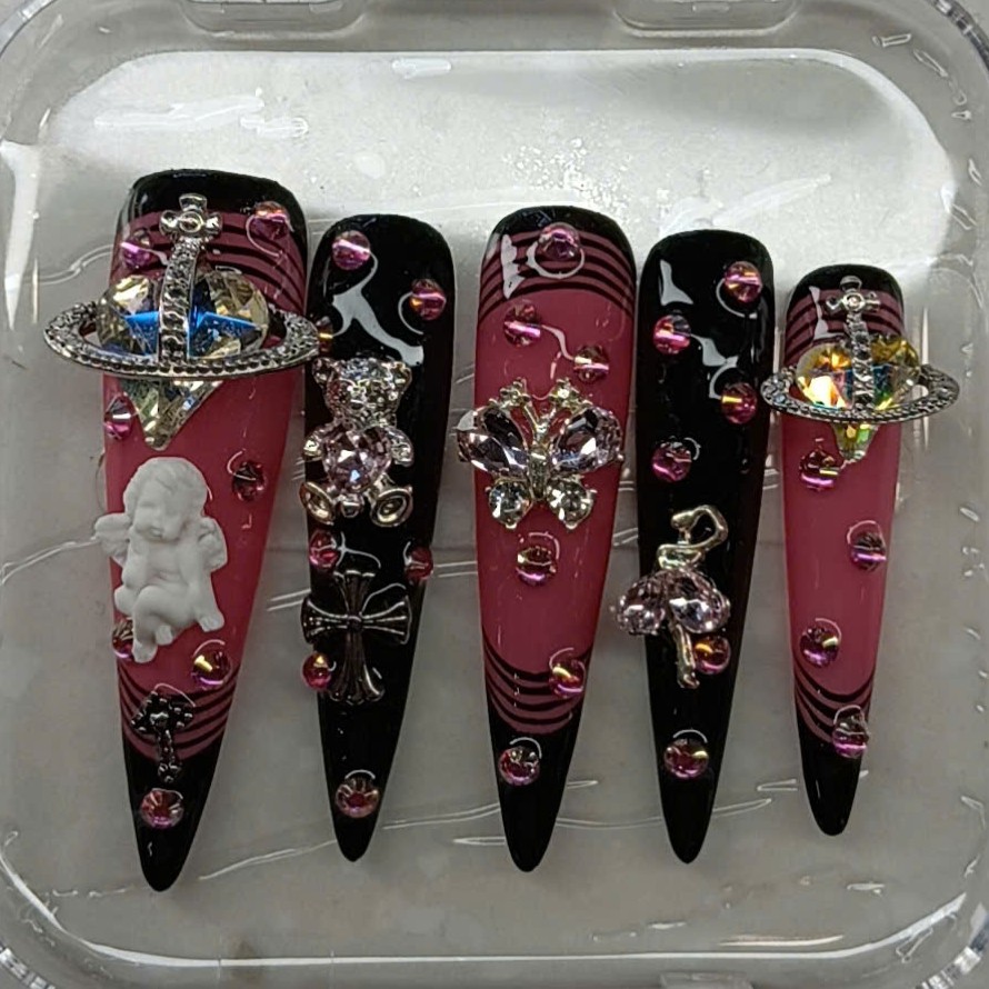 Long stiletto Y2K press-on nails in black and pink featuring 3D planet orb, cherub, cross, and teddy bear charms by Pro Nails