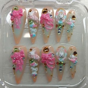 Long stiletto press-on nails featuring 3D white bunnies, pink ribbons, carousel horses, and rhinestones by Pro Nails