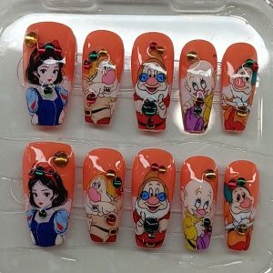 Bright orange press-on nails featuring Snow White and the Seven Dwarfs character art with colorful rhinestones by Pro Nails